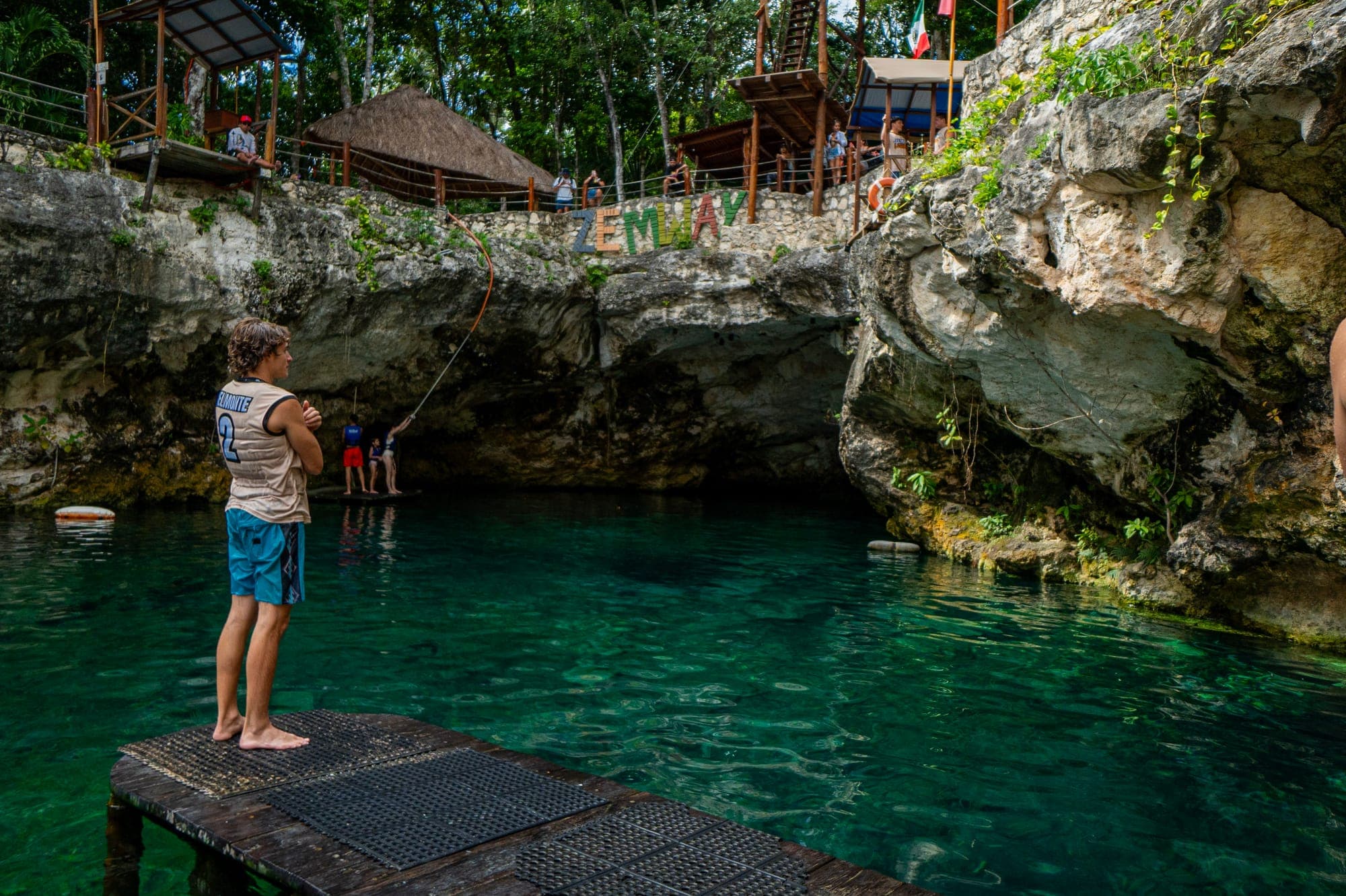 A visitor standing on a wooden platform, looking out over a turquoise cenote